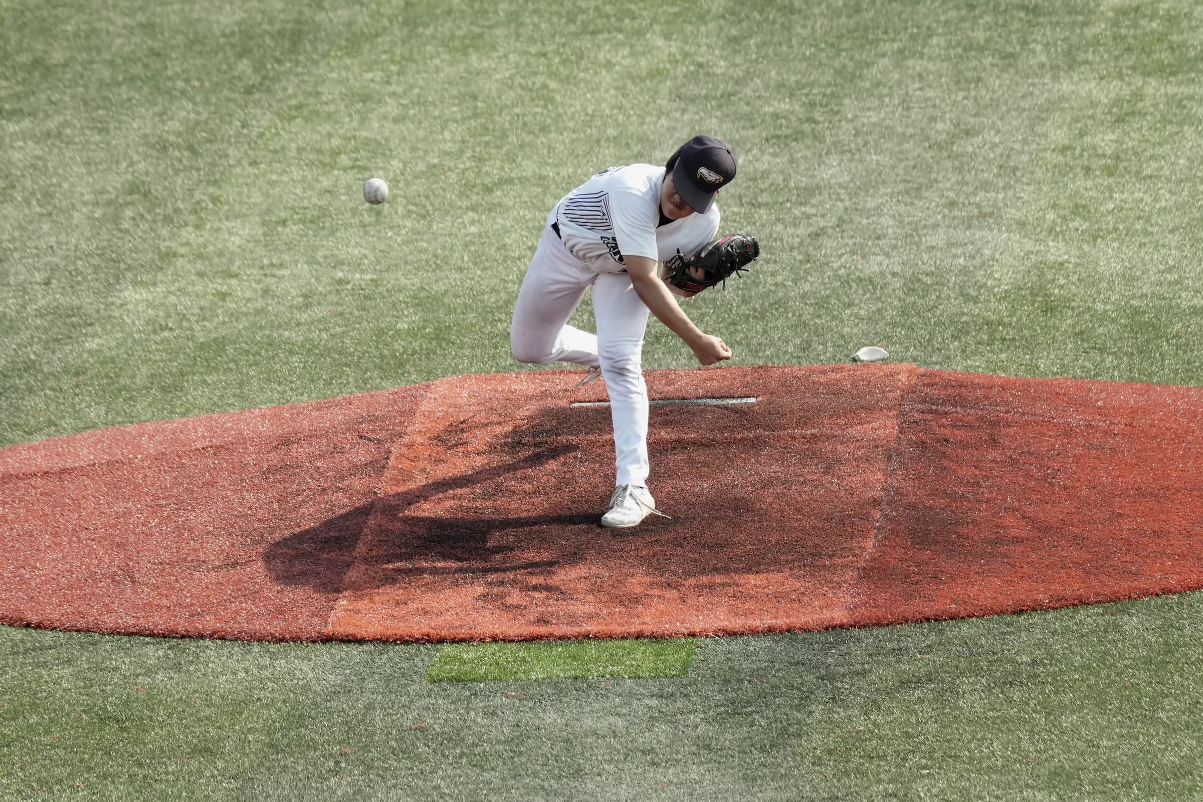 A pitcher follows through on the mound as the baseball travels toward the plate.
